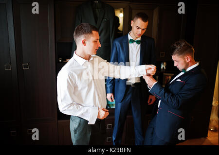 Groomsmen aiutare lo sposo a vestire e preparatevi per la sua cerimonia nuziale. Foto Stock