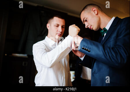 Groomsmen aiutare lo sposo a vestire e preparatevi per la sua cerimonia nuziale. Foto Stock