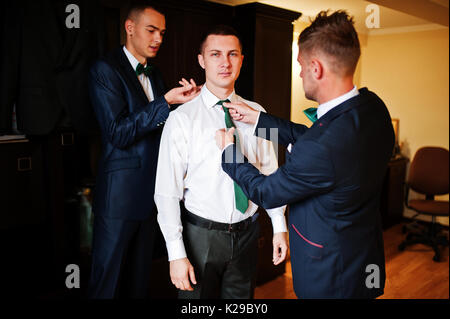 Groomsmen aiutare lo sposo a vestire e preparatevi per la sua cerimonia nuziale. Foto Stock