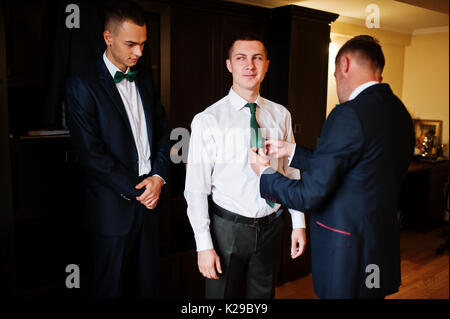 Groomsmen aiutare lo sposo a vestire e preparatevi per la sua cerimonia nuziale. Foto Stock