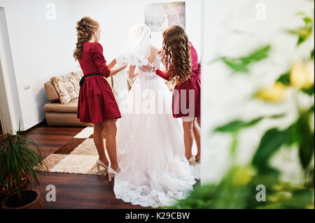 Bridesmaids aiutando sposa per legare un archetto su un abito da sposa. Foto Stock