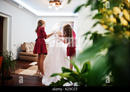 Bridesmaids aiutando sposa per legare un archetto su un abito da sposa. Foto Stock