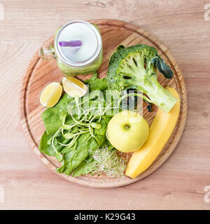 Verdure fresche a foglia verde e verde smoothie in barattolo. Detox, la dieta o il cibo sano concetto. Mason jar dietetico di drink con broccoli, spinaci, microgreens, calce e banana su sfondo di legno. Vista dall'alto. Foto Stock