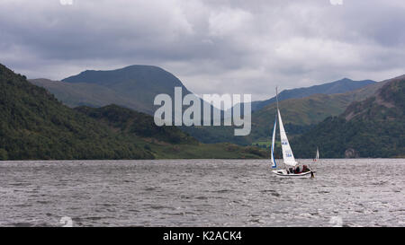 Da dolci colline e sotto il cielo grigio, le persone sono la vela in piccole barche a Ullswater - vista a Glenridding & Patterdale, Lake District, Inghilterra, Regno Unito. Foto Stock