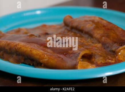 Chiudere fino a tre formaggi enchiladas su un bel piatto di colore blu Foto Stock