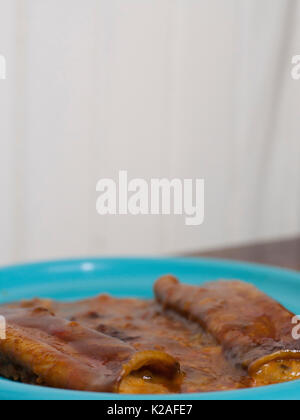 Chiudere fino a tre formaggi enchiladas su un bel piatto di colore blu Foto Stock