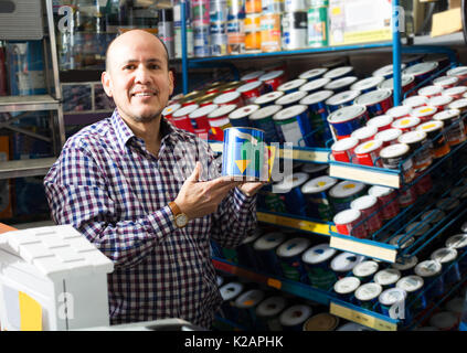 Sorridente pensionato maschio scegliendo il colore della vernice nel supermercato Foto Stock