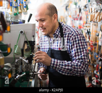 Sorridente uomo maturo nel piazzale di sosta nel lavoro di fabbro e rendendo i duplicati di chiavi Foto Stock