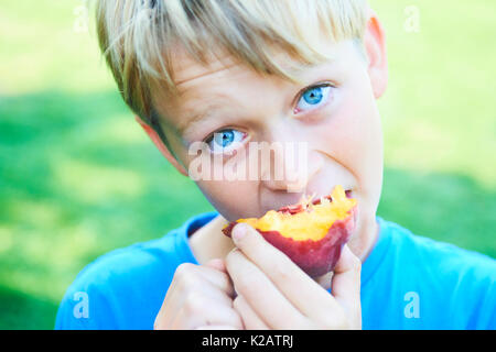 Ritratto di bambino ragazzo mangiare peach. bambino felice in sun giorno d'estate. il capretto con frutto nella natura dello sfondo. Foto Stock