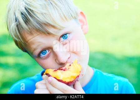 Ritratto di bambino ragazzo mangiare peach. bambino felice in sun giorno d'estate. il capretto con frutto nella natura dello sfondo. Foto Stock