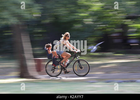 Sofia, Bulgaria - 20 agosto 2017 - una giovane donna e di sua figlia un giro in bici nel Parco. Slow motion con sfondo sfocato degli alberi. Foto Stock