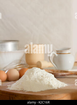 La farina di frumento bianca e le materie prime per le uova di gallina per preparare la pasta e utensili da cucina contro una parete bianca. Concetto di cucina rustica, messa a fuoco selettiva. Cop Foto Stock