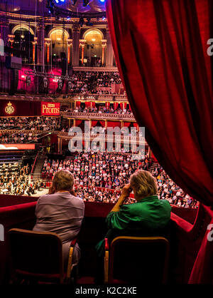 ALBERT HALL INTERNO BBC Proms prestazioni con colleghe in primo piano la visione di musica le prestazioni utilizzando occhiali opera insediato nel lusso in velluto rosso casella privato con platea e palco orchestra palco in background Foto Stock