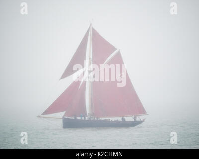 Un unico pilota in legno taglierina classic yacht barca red sails vela su acque calme in densa nebbia foggy nebbia grigio grigio cielo scarsa visibilità cattivo tempo Foto Stock