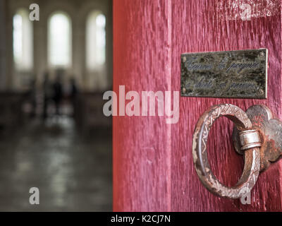 Un rosso in legno chiesa cappella porta apertura chiusura socchiusa con ferro tondo in ottone anello a tirare la maniglia e placca avviso persone all altare Foto Stock