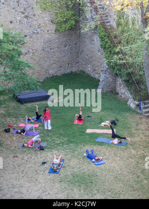 Yogi esercizi yoga insegnante insegnamento tenendo una classe in un cerchio esterno al fresco nel giardino murato prato in ombra lontano dal sole e il calore Foto Stock