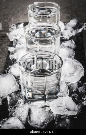 Alcol e cocktail. Tre Bicchieri di vodka su un vassoio di ardesia, con ghiaccio. Su una pietra nera tabella, Foto Stock