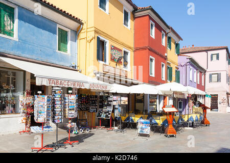 Brighty negozi colorati in Burano main street, Venezia, Veneto, Italia con un negozio di souvenir per i turisti a fianco di una tradizionale trattoria o ristorante. Foto Stock