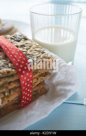 Closeup colpo di nastrare con striscia rossa pila di biscotti fatti da sfoglia di impasto coperto con il girasole, chia e i semi di sesamo e il bicchiere di latte Foto Stock
