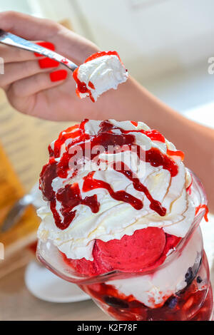 La donna tiene un cucchiaio e gusto delizioso gelato alla fragola con frutta in una grande ciotola di vetro in un ristorante Foto Stock