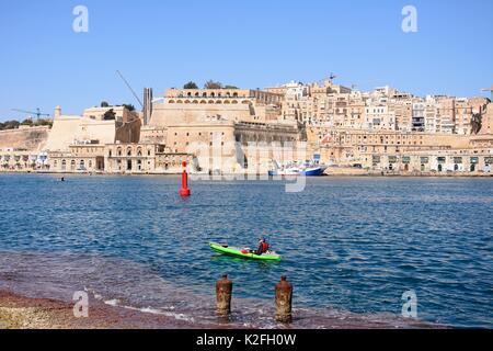 La Valletta Waterfront edifici tra cui Upper Barrakka Gardens viste attraverso il Grand Harbour in Vittoriosa con un canoeist in primo piano, Val Foto Stock