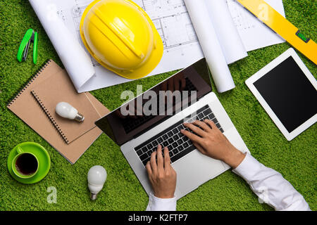 Il luogo di lavoro con casco, blueprint, laptop e blocco note su sfondo di erba. Vista da sopra con lo spazio di copia Foto Stock