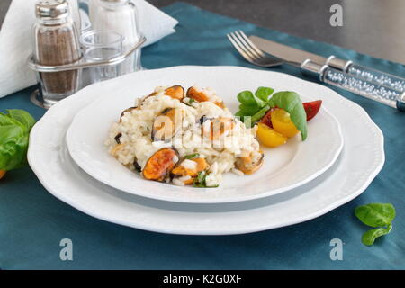Risotto con le cozze su una piastra bianca con basilico, pomodori ciliegia su un panno verde. Mangiare sano concetto, Meditarranian stile di vita Foto Stock