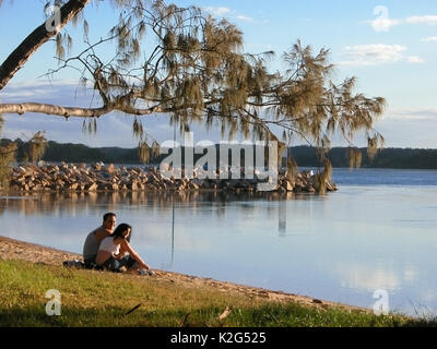 Giovane seduto sulla spiaggia fluviale alla sera, Nambucca River, Nambucca capi, NSW, Australia Foto Stock