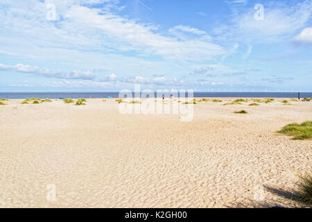 Su di una larga spiaggia di Caister-su-Mare con un piccolo gruppo di persone in distanza. Fino al mare sono le turbine eoliche. Foto Stock