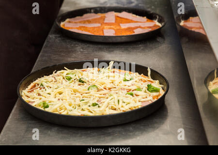 Due black metal lastre di cottura a crudo con pizza sul tavolo della cucina del ristorante o bar. La prima pizza fatta con verdure e formaggio grattugiato, un Foto Stock