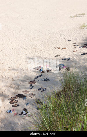 Sandali, infradito & scarpe a sinistra nella sabbia dai piedi nudi beachgoers. Foto Stock