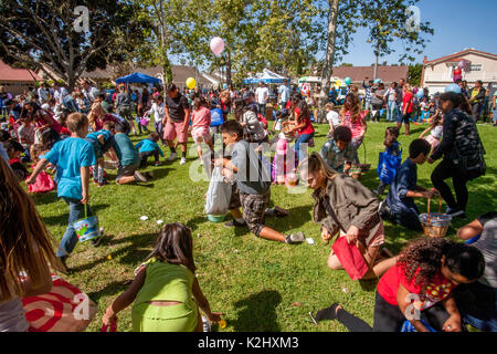 Multirazziale bambini che portano ceste sciame attraverso il prato di un parco in Costa Mesa, CA, ricerca di dispersi premi pasquali. Foto Stock