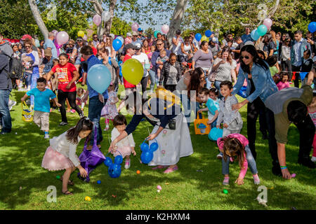 Multirazziale bambini che portano ceste sciame attraverso il prato di un parco in Costa Mesa, CA, ricerca di dispersi premi pasquali. Foto Stock