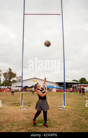 Un kilted giovane donna compete nel 'Sheaf Toss' in corrispondenza di un festival scozzese in Costa Mesa, CA, utilizzando un forcone per mescolare un 16-pound borsa di tela di paglia su una barra. Foto Stock