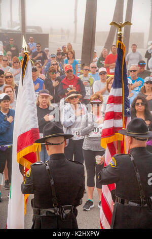 Multirazziale mogli militare di salutare la bandiera noi pur riconoscendo un omaggio da spettatori e partecipanti prima di competere in una gara podistica in Huntington Beach, CA. Foto Stock