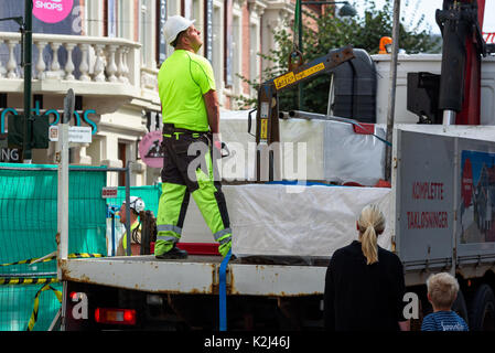 Kristiansand, Norvegia - 16 agosto 2017: Travel documentario del lavoratore edile sul pianale di un autocarro, in procinto di iniziare un sollevamento di plasterboards wi Foto Stock