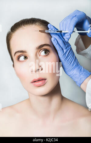 Medico aesthetician in blu guanti medicali rende acido ialuronico iniezioni di bellezza sulla fronte del paziente femmina Foto Stock