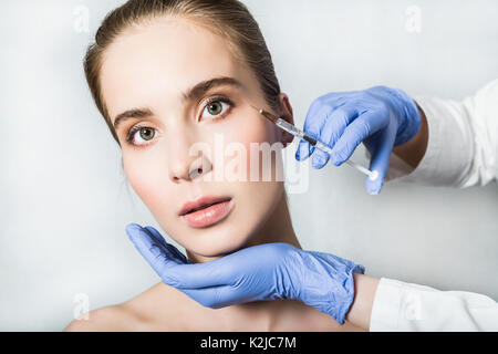 Medico aesthetician in blu guanti medicali rende acido ialuronico iniezioni di bellezza nella periorbitale aree del giovane paziente femmina Foto Stock