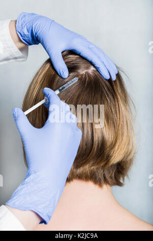 Medico aesthetician in blu guanti medicali rende acido ialuronico ringiovanimento iniezioni di bellezza nella parte posteriore della testa del paziente di sesso femminile per capelli gro Foto Stock