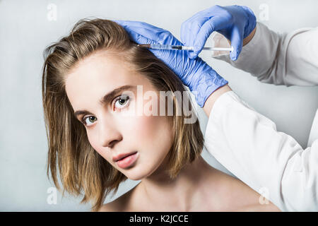 Medico aesthetician in blu guanti medicali rende acido ialuronico ringiovanimento iniezioni di bellezza nella parte posteriore della testa della bella giovane femmina pati Foto Stock