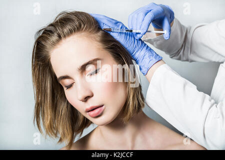 Medico aesthetician in blu guanti medicali rende acido ialuronico ringiovanimento iniezioni di bellezza nella parte posteriore della testa della bella paziente femmina fo Foto Stock