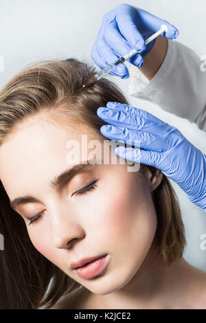 Medico aesthetician in blu guanti medicali rende acido ialuronico ringiovanimento iniezioni di bellezza nella parte posteriore della testa della bella giovane femmina pati Foto Stock