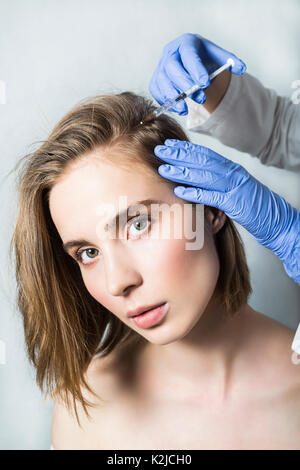 Medico aesthetician in blu guanti medicali rende acido ialuronico ringiovanimento iniezioni di bellezza nella parte posteriore della testa del paziente di sesso femminile per capelli gro Foto Stock