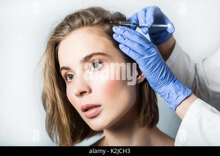 Medico aesthetician in blu guanti medicali rende acido ialuronico ringiovanimento iniezioni di bellezza nella parte posteriore della testa della bella giovane femmina pati Foto Stock