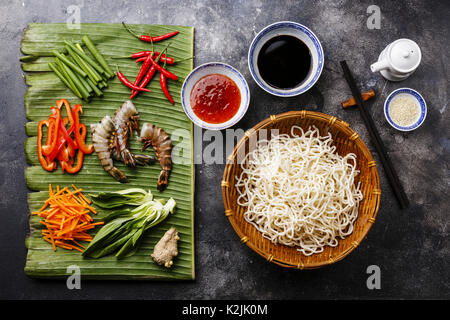 Ingredienti per la cottura di Udon tagliatelle con gamberi tigre, verdi, verdure, spezie su foglia di banana su sfondo scuro Foto Stock