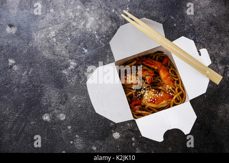 Udon Noodles saltati in padella con gamberi tigre asiatica nella casella estrarre cibo su sfondo scuro spazio copia Foto Stock