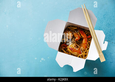 Udon Noodles saltati in padella con gamberi tigre asiatica nella casella estrarre cibo su sfondo blu spazio copia Foto Stock