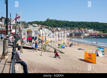 RNLI stazione bagnino capanna e persone visitatori turisti in estate South Bay Scarborough Beach North Yorkshire Inghilterra Regno Unito Gran Bretagna Foto Stock