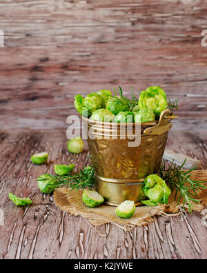 Green materie cavoletti di Bruxelles in una ciotola di legno su una tavola in legno rustico, il fuoco selettivo Foto Stock