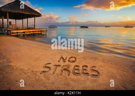 Primo piano scritto nella sabbia 'No stress' al tramonto in isola Maurizio con Jetty silhouette e le barche dei pescatori in background. Foto Stock